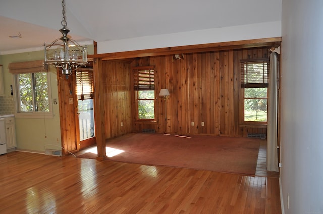 unfurnished dining area with wood walls, a notable chandelier, and light wood-type flooring