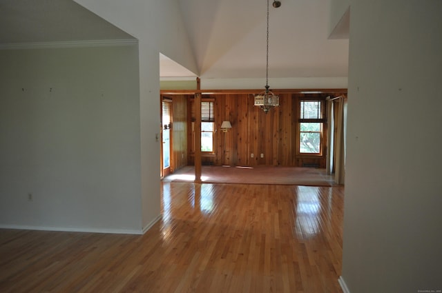 unfurnished dining area featuring crown molding, wood finished floors, baseboards, a notable chandelier, and wooden walls