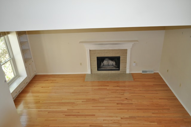 unfurnished living room with visible vents, baseboards, a tiled fireplace, and light wood-type flooring