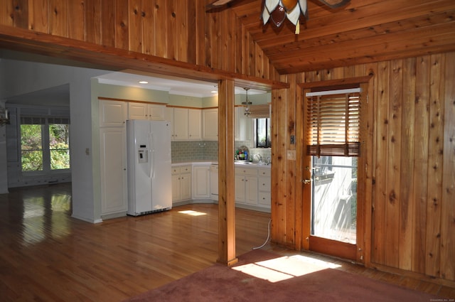 kitchen with wood walls, white refrigerator with ice dispenser, white cabinets, a ceiling fan, and vaulted ceiling