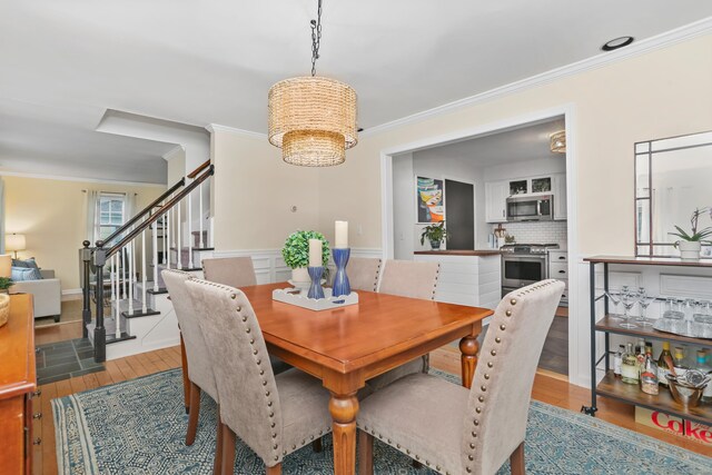 dining area with wood finished floors, stairway, ornamental molding, and a chandelier