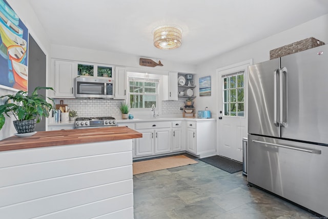 kitchen featuring stainless steel appliances, open shelves, butcher block countertops, a sink, and decorative backsplash