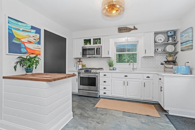 kitchen featuring appliances with stainless steel finishes, open shelves, a sink, and decorative backsplash