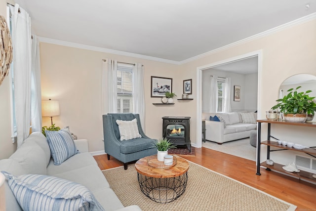living room featuring healthy amount of natural light, wood finished floors, crown molding, a wood stove, and baseboards