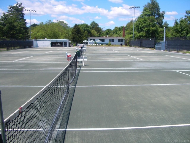 view of tennis court featuring community basketball court, fence, and view of wooded area