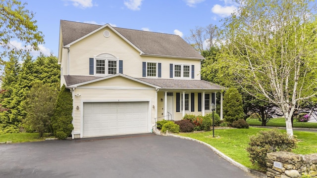 traditional-style home featuring covered porch, roof with shingles, a front yard, and driveway