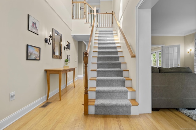 staircase with baseboards, crown molding, visible vents, and wood-type flooring