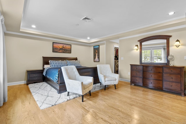bedroom with a tray ceiling, visible vents, wood finished floors, and baseboards