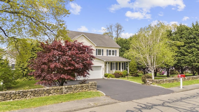 traditional home with an attached garage, driveway, and a front lawn