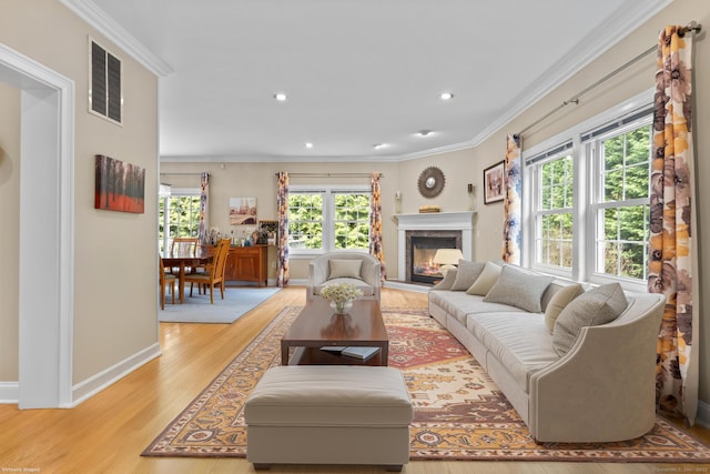 living area with visible vents, baseboards, a glass covered fireplace, light wood-style floors, and ornamental molding