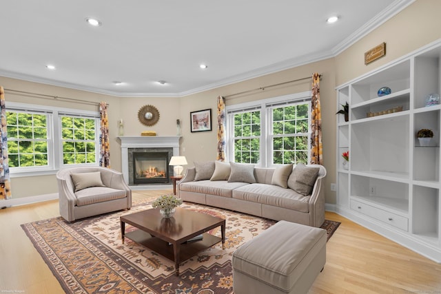living area featuring crown molding, light wood-type flooring, baseboards, a glass covered fireplace, and recessed lighting