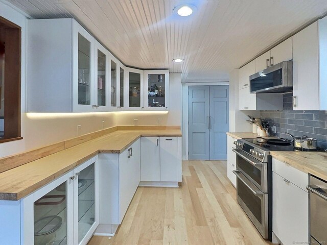 kitchen with appliances with stainless steel finishes, light wood-type flooring, white cabinetry, glass insert cabinets, and recessed lighting