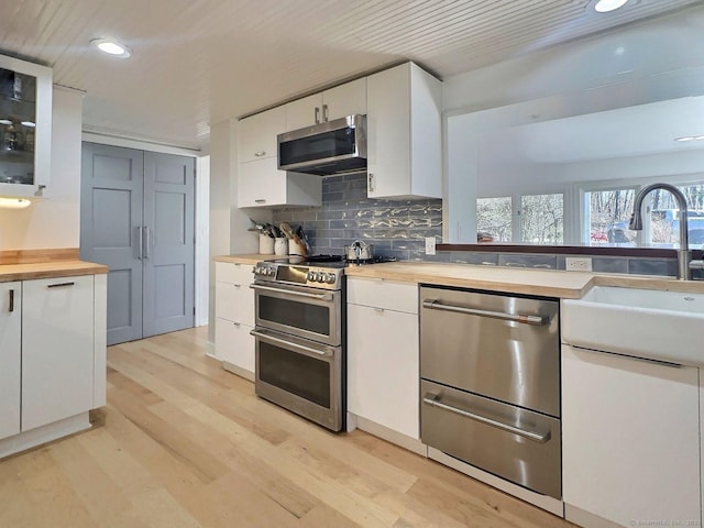 kitchen featuring appliances with stainless steel finishes, wood counters, recessed lighting, light wood finished floors, and white cabinetry