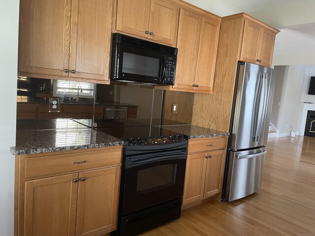 kitchen with dark stone counters, light wood finished floors, and black appliances