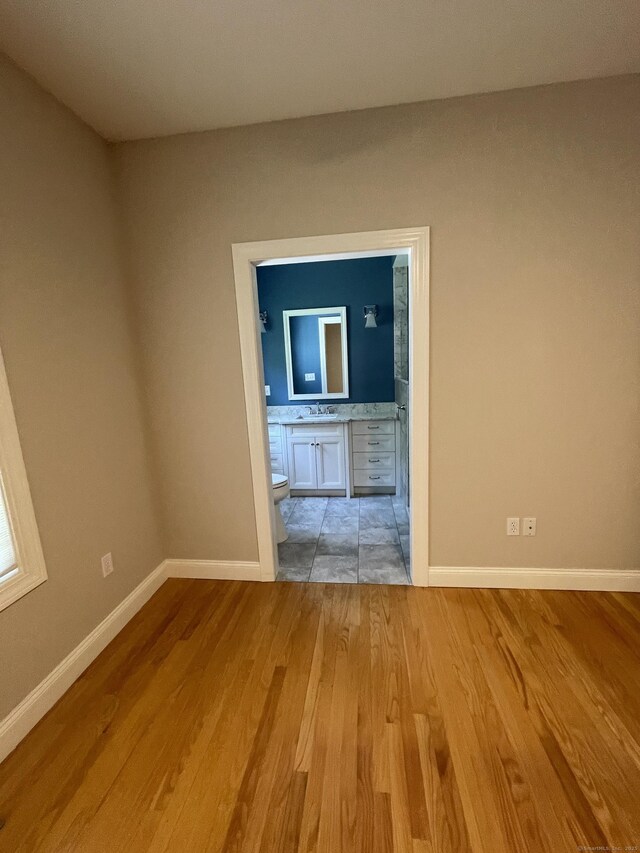 unfurnished room with light wood-style floors, a sink, and baseboards