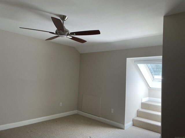empty room with light colored carpet, a ceiling fan, baseboards, and vaulted ceiling with skylight