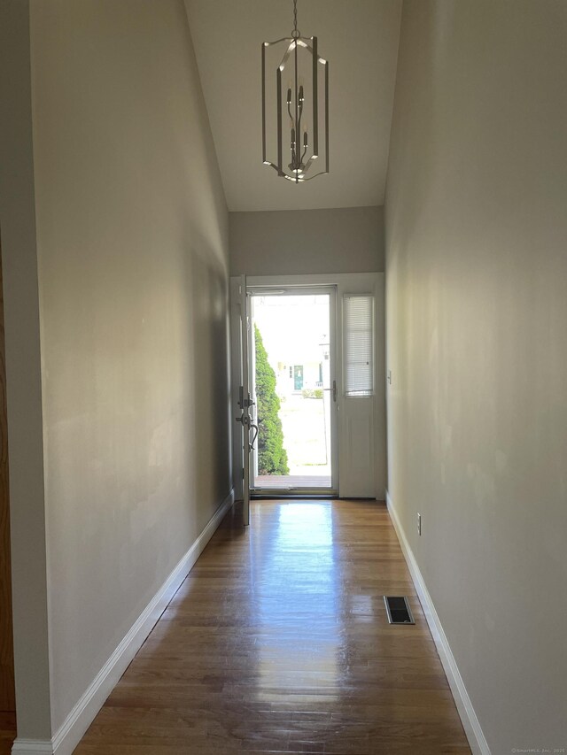 doorway with baseboards, a notable chandelier, visible vents, and wood finished floors