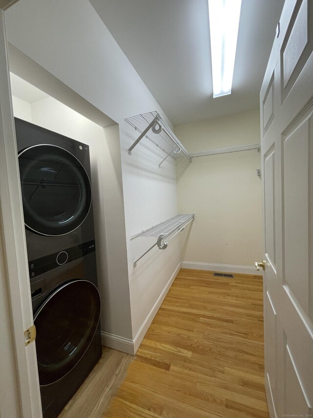 washroom featuring baseboards, laundry area, stacked washer / dryer, and light wood finished floors