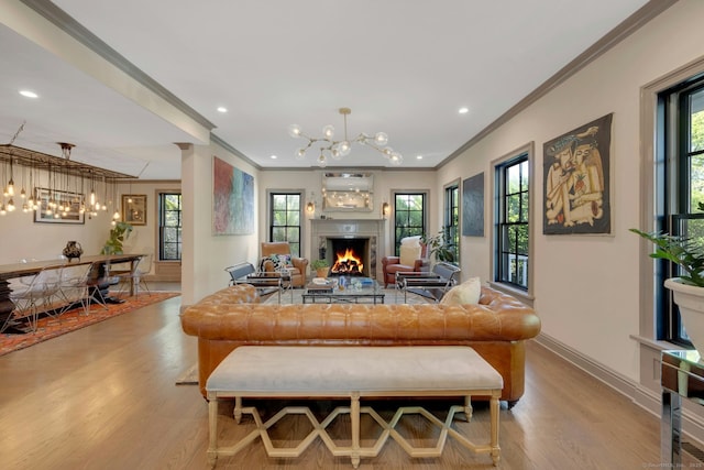 living room featuring crown molding, wood finished floors, a healthy amount of sunlight, a lit fireplace, and a chandelier