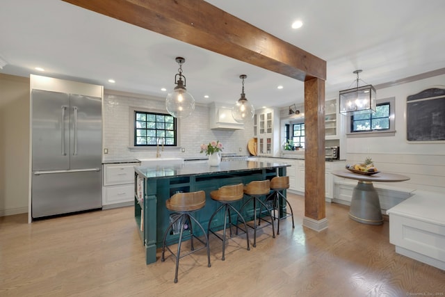 kitchen featuring white cabinets, stainless steel built in refrigerator, tasteful backsplash, a kitchen bar, and glass insert cabinets