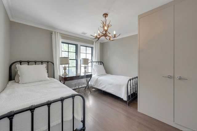 bedroom featuring a chandelier, ornamental molding, wood finished floors, and visible vents