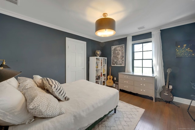 bedroom with crown molding, baseboards, wood finished floors, and visible vents