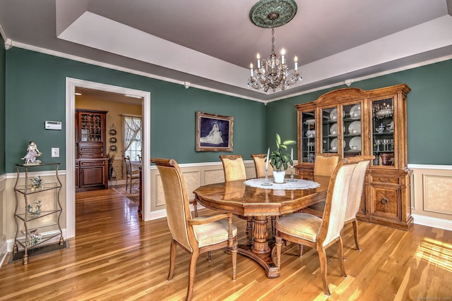 dining room featuring an inviting chandelier, a decorative wall, a wainscoted wall, light wood-type flooring, and a tray ceiling