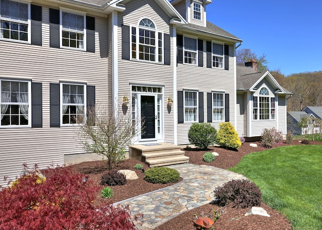 colonial house featuring roof with shingles and a front lawn