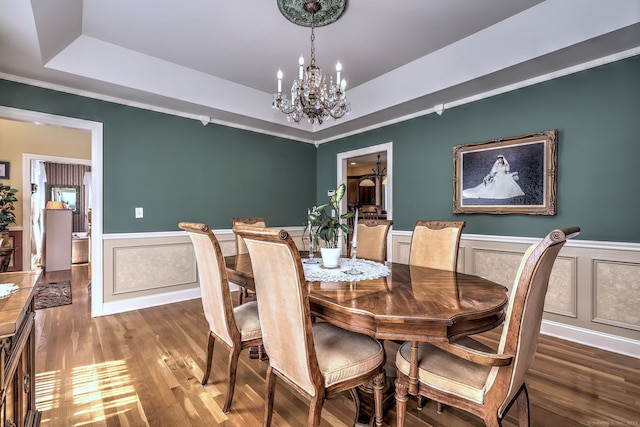 dining room featuring crown molding, wood finished floors, a wainscoted wall, a chandelier, and a tray ceiling