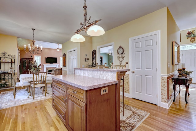 kitchen with a kitchen bar, brown cabinets, light countertops, light wood finished floors, and a notable chandelier