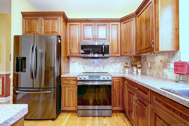 kitchen featuring appliances with stainless steel finishes, light wood-type flooring, and brown cabinets