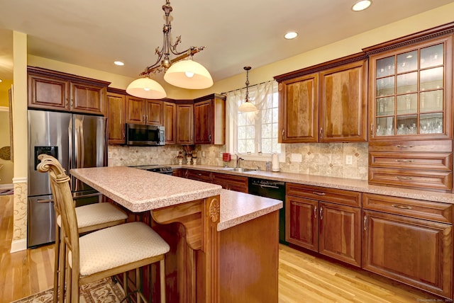 kitchen with appliances with stainless steel finishes, a breakfast bar, a sink, light wood-style floors, and light countertops