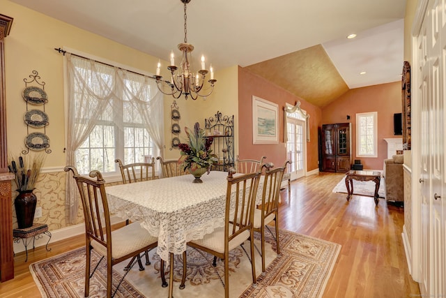 dining space with baseboards, an inviting chandelier, lofted ceiling, and light wood-type flooring