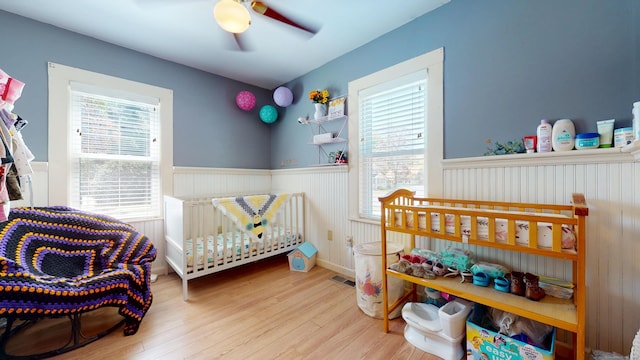 bedroom with a wainscoted wall, wood finished floors, and a ceiling fan