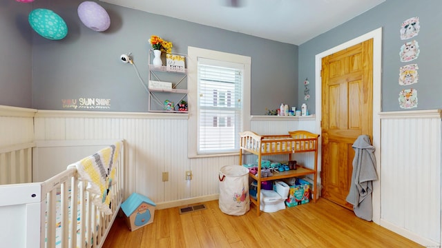 bedroom with wood finished floors, a wainscoted wall, and baseboards