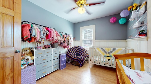 bedroom featuring wainscoting, light wood finished floors, and ceiling fan