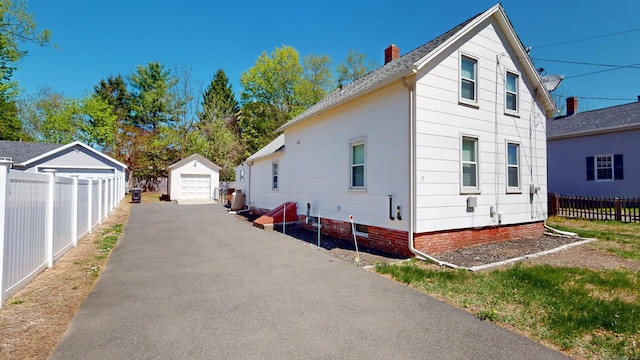 view of side of home featuring fence, a garage, a chimney, asphalt driveway, and an outbuilding