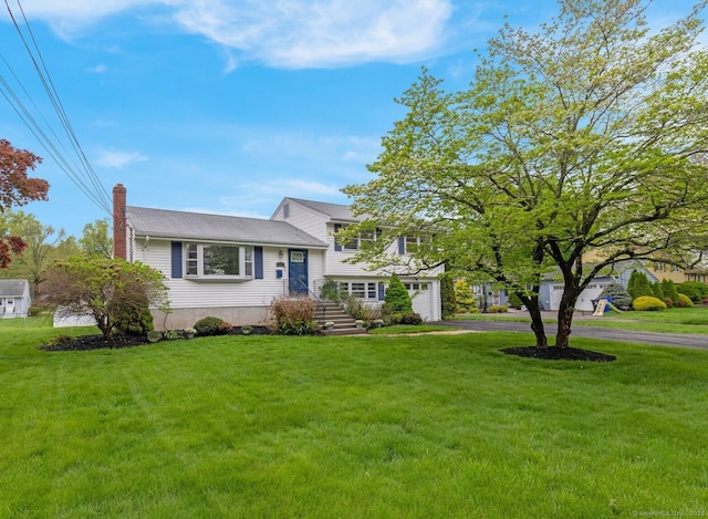 tri-level home featuring a chimney, driveway, a front lawn, and an attached garage