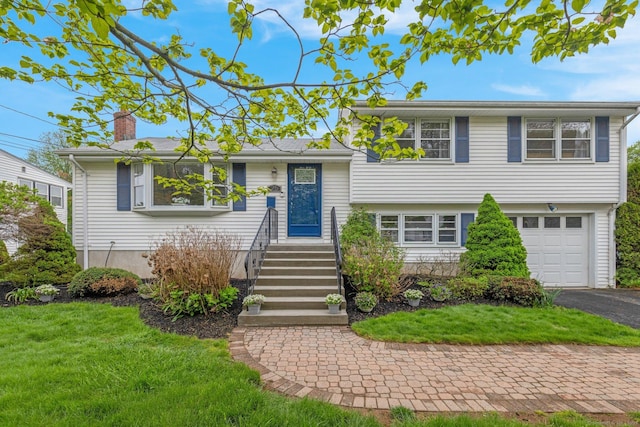 split level home with a chimney, a garage, driveway, and a front lawn