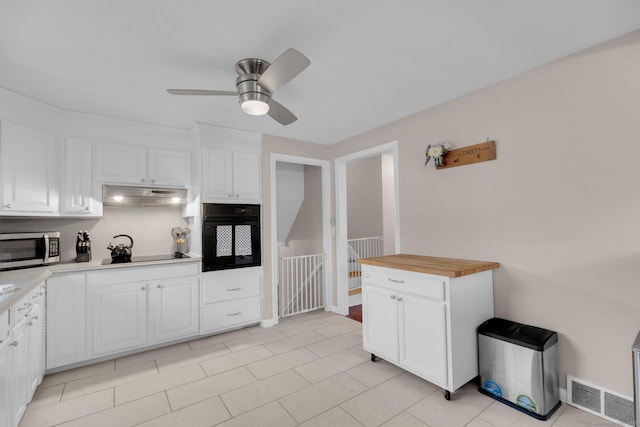 kitchen with black appliances, under cabinet range hood, ceiling fan, white cabinets, and light tile patterned floors