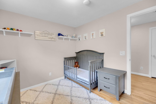 bedroom featuring wood finished floors, baseboards, and a nursery area