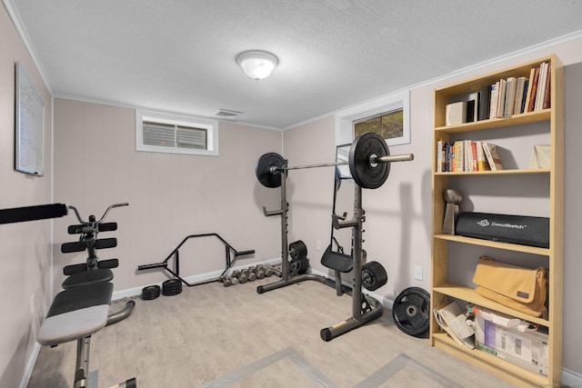 exercise area featuring wood finished floors, ornamental molding, a textured ceiling, and baseboards