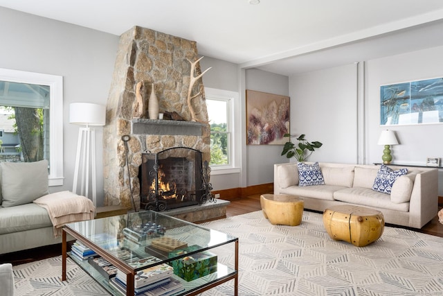 living room featuring baseboards, plenty of natural light, a stone fireplace, and wood finished floors