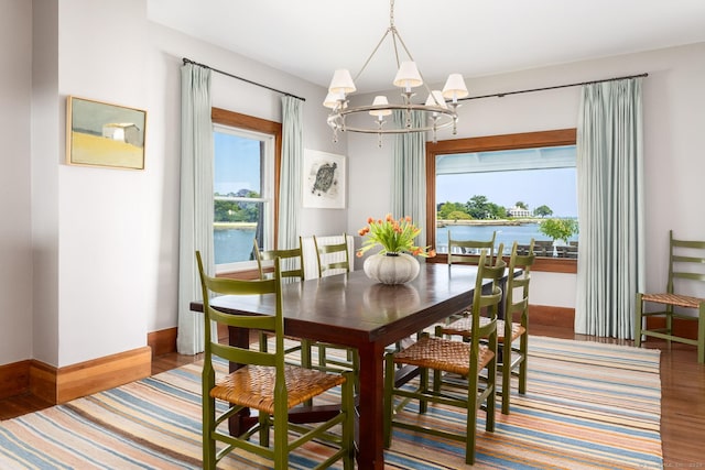 dining area featuring a water view, baseboards, a notable chandelier, and wood finished floors