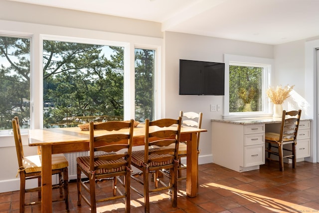 dining space featuring built in desk, dark tile patterned flooring, baseboards, and a wealth of natural light