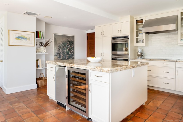 kitchen with visible vents, beverage cooler, a center island, stainless steel double oven, and wall chimney exhaust hood