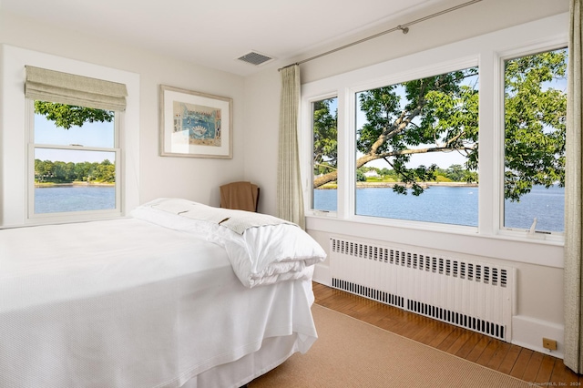 bedroom with visible vents, radiator, a water view, and wood finished floors