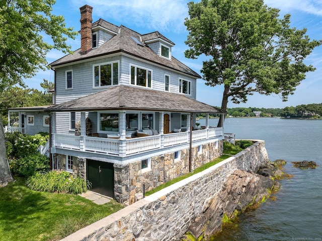 view of front facade with a water view, a chimney, a balcony, and stone siding