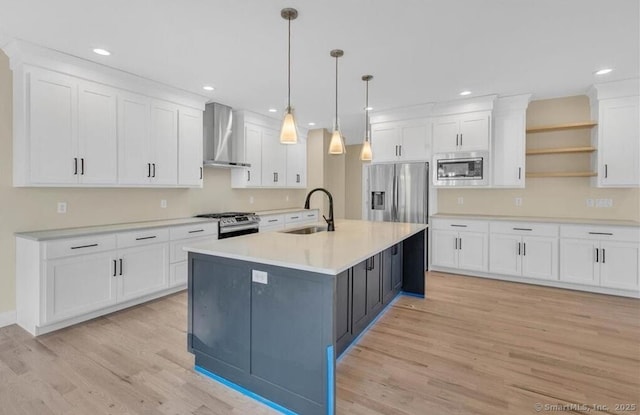 kitchen featuring wall chimney range hood, appliances with stainless steel finishes, light wood-type flooring, a sink, and white cabinetry