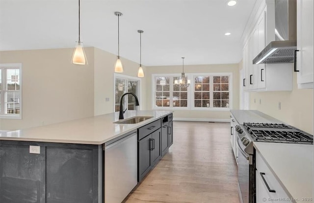 kitchen with white cabinets, appliances with stainless steel finishes, a sink, light wood-style floors, and wall chimney exhaust hood
